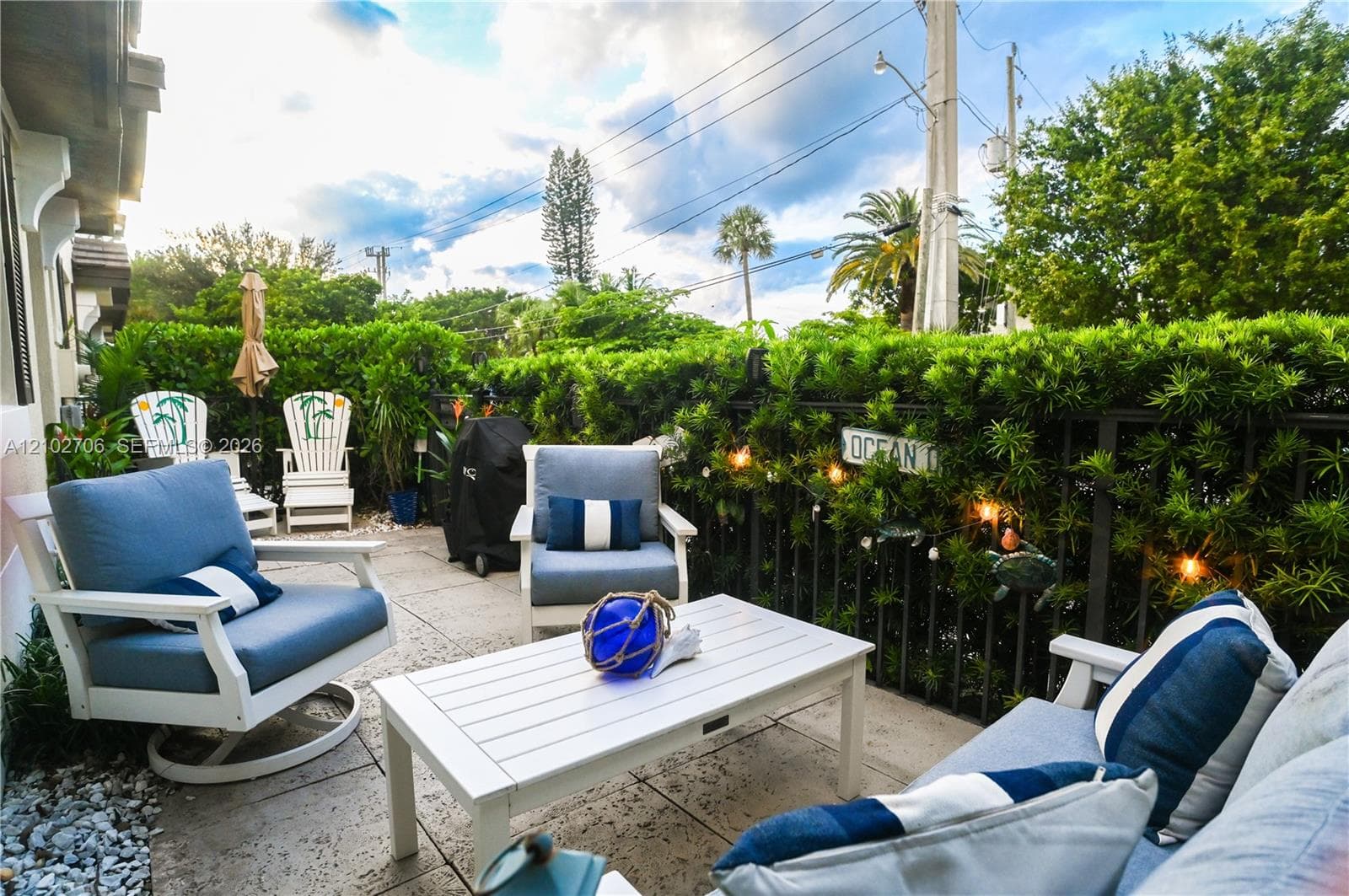 Private patio featuring stone pavers and perimeter metal fencing encased in mature privacy hedges