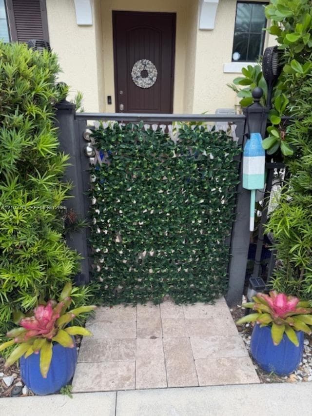 Private entryway featuring a stone-tile walkway, decorative metal gate, and manicured landscaping