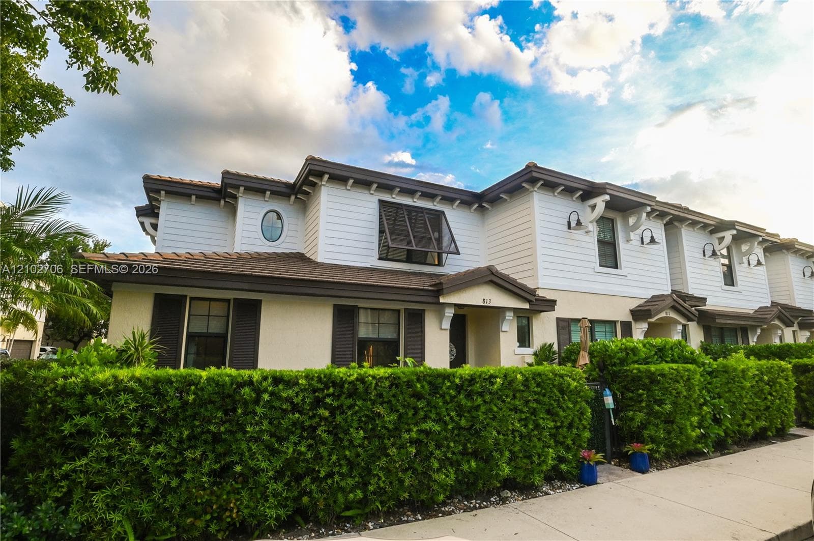 Two-story exterior featuring a mix of horizontal lap siding and stucco, dark-toned roof shingles, decorative exterior wall-mounted lighting, and an oval accent window