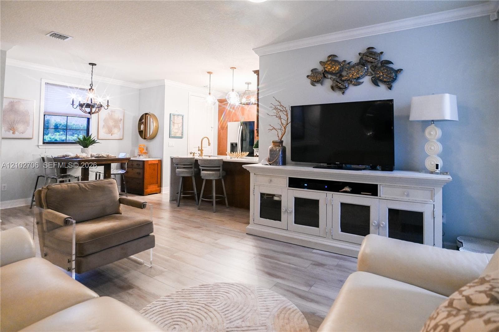 Open-concept interior featuring light-toned wood-finish flooring, crown molding, a kitchen island with bar seating, and decorative chandelier lighting