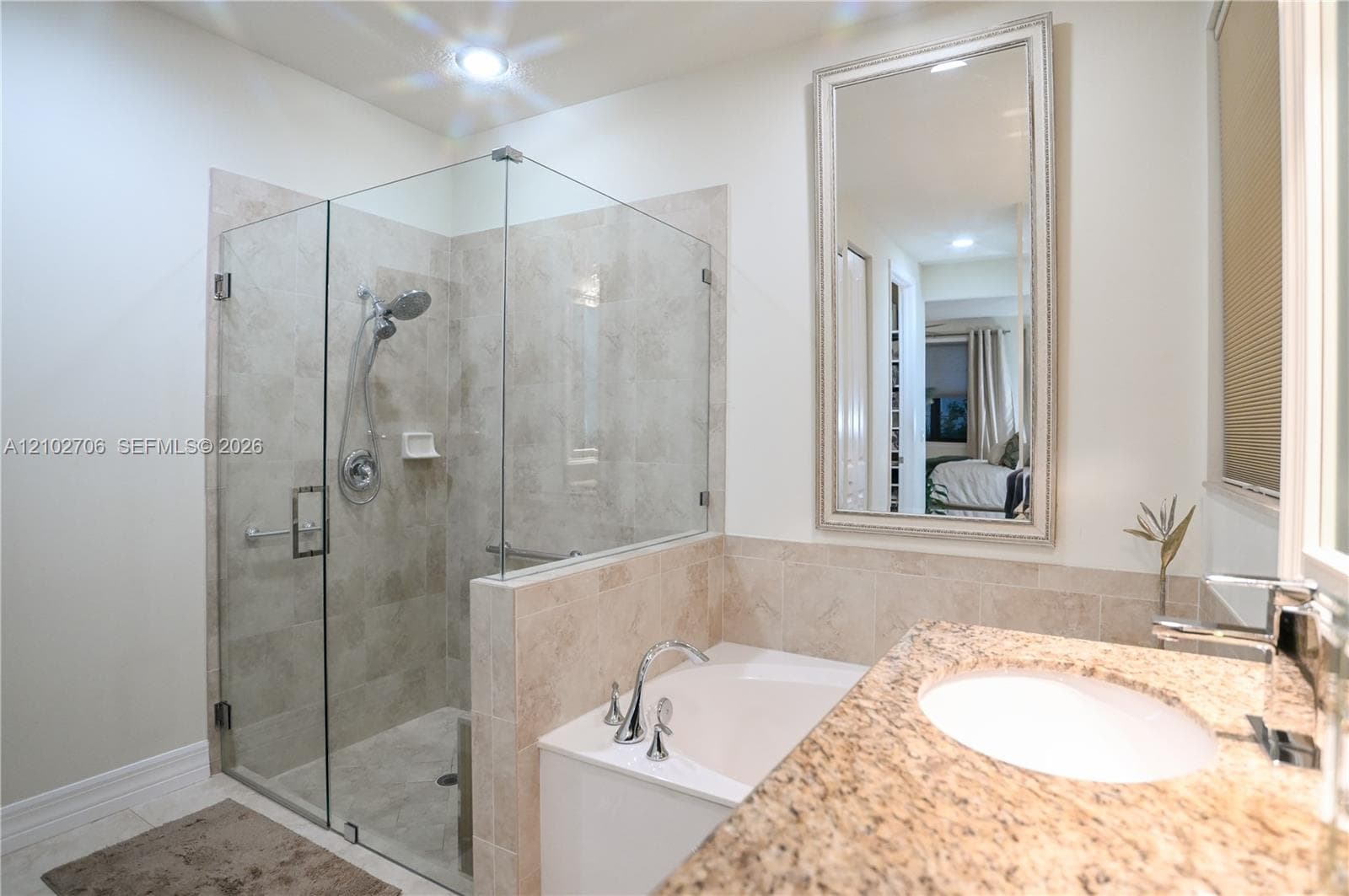 Stone-topped vanity with an undermount sink, framed wall mirror, deep soaking tub, and separate glass-enclosed shower with tiled surrounds
