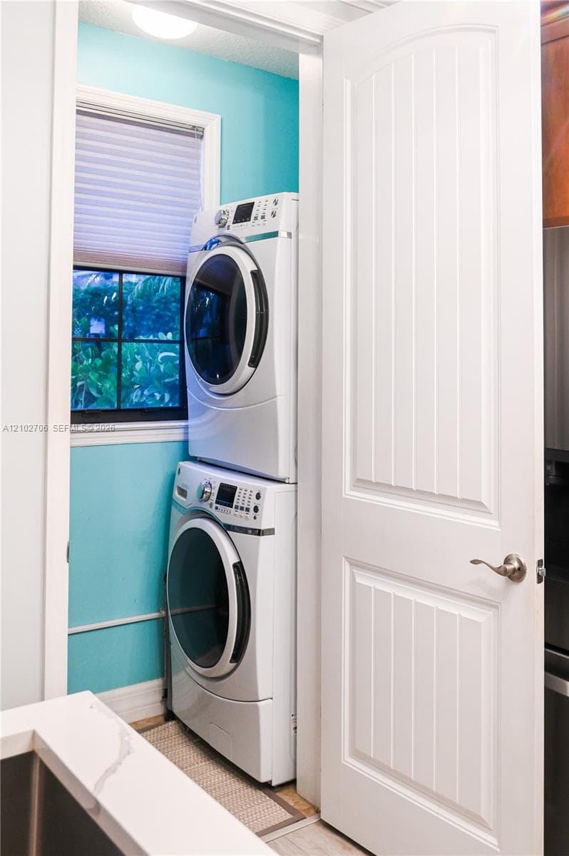 Dedicated laundry space featuring a stacked washer and dryer, single-pane window with grid muntins, and a multi-panel interior door with brushed-metal hardware