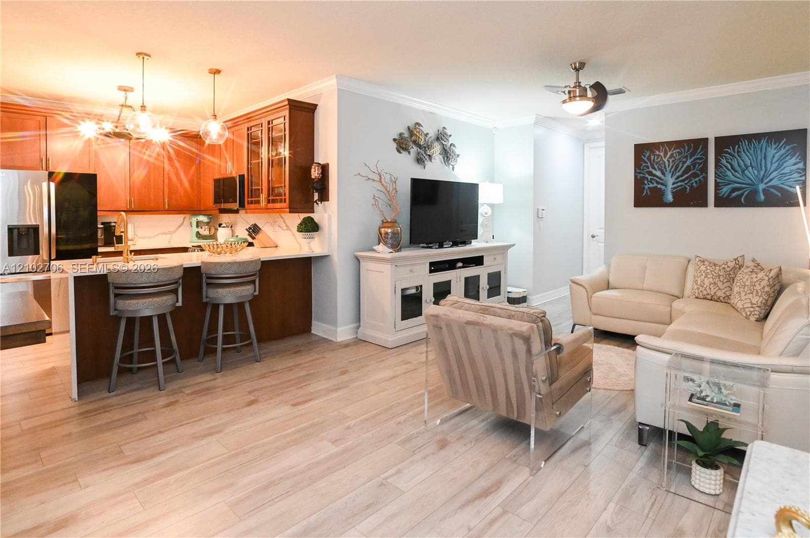 Open-concept interior featuring wood-finish flooring, a kitchen island with quartz countertops, custom cabinetry with glass-panel accents, crown molding, and a ceiling fan with integrated lighting