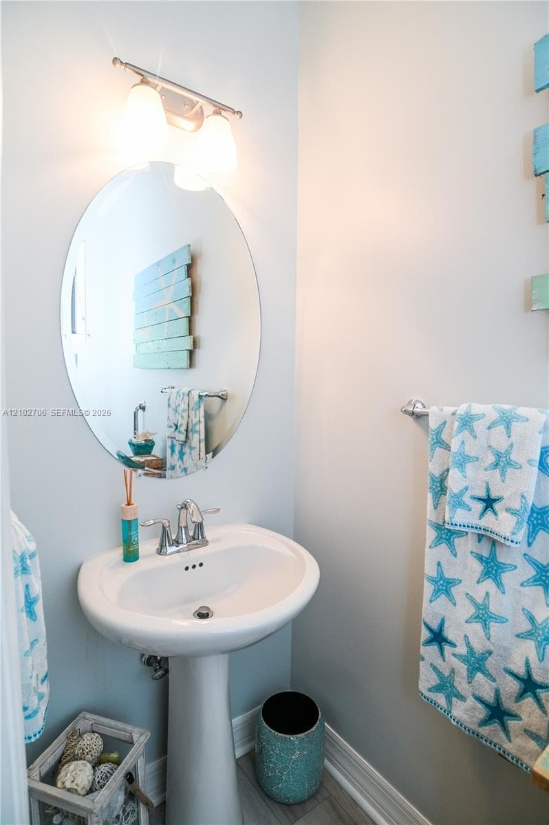 White pedestal sink featuring a dual-handle chrome faucet, oval wall-mounted mirror, and multi-bulb vanity light fixture