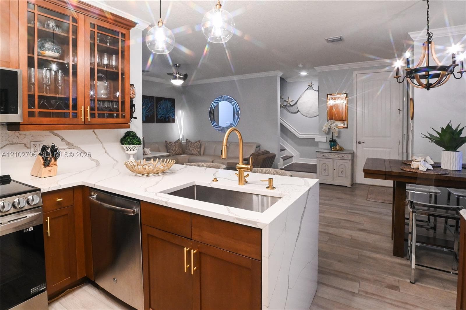 Kitchen featuring wood cabinetry, stone-finish countertops with waterfall edge, stainless steel undermount sink, brass-finish faucet, and wood-finish flooring