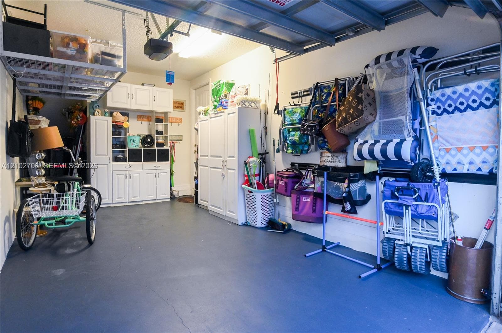 Garage featuring painted flooring, white built-in cabinetry, overhead ceiling storage rack, and a wall-mounted storage track system