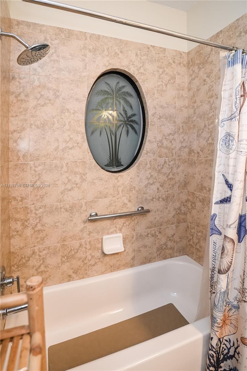 Shower and tub combination with neutral-toned wall tile, oval-shaped decorative accent window, integrated metal grab bar, and wall-mounted soap dish