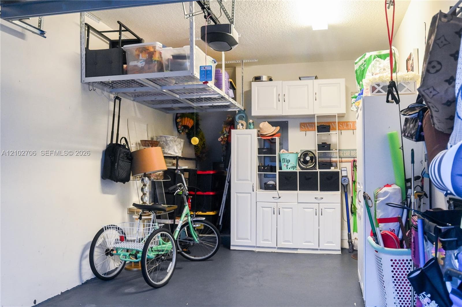 Garage interior featuring built-in white cabinetry, wall-mounted storage units, and overhead ceiling-mounted shelving