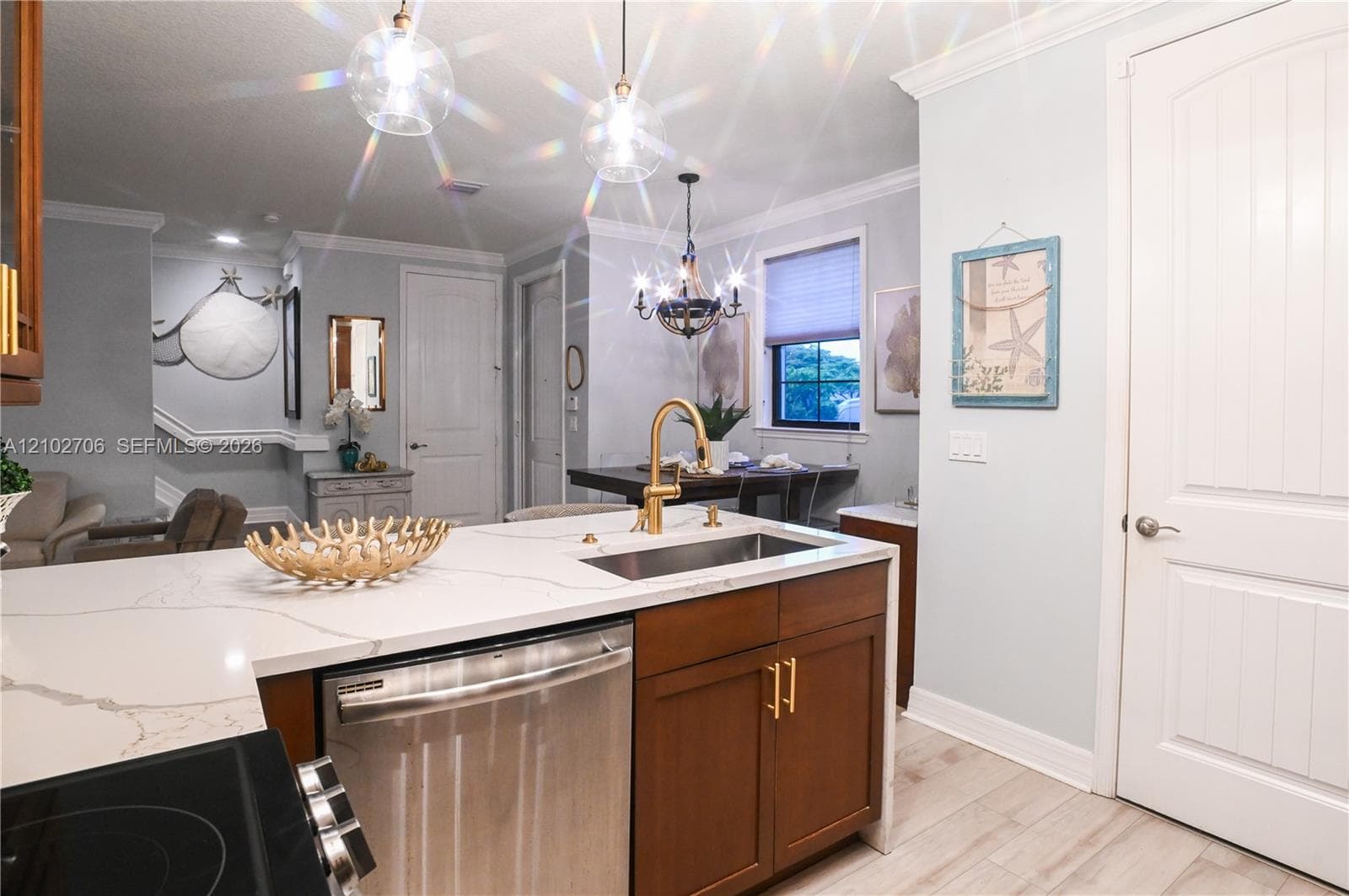 Kitchen featuring a quartz countertop, stainless steel under-mount sink, brass-finish gooseneck faucet, shaker-style cabinetry with gold-tone hardware, and wood-finish flooring