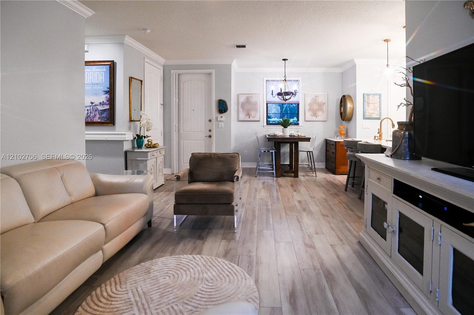 Wood-finish flooring, crown molding, arched-top interior door, kitchen island with metallic faucet, and decorative overhead chandelier