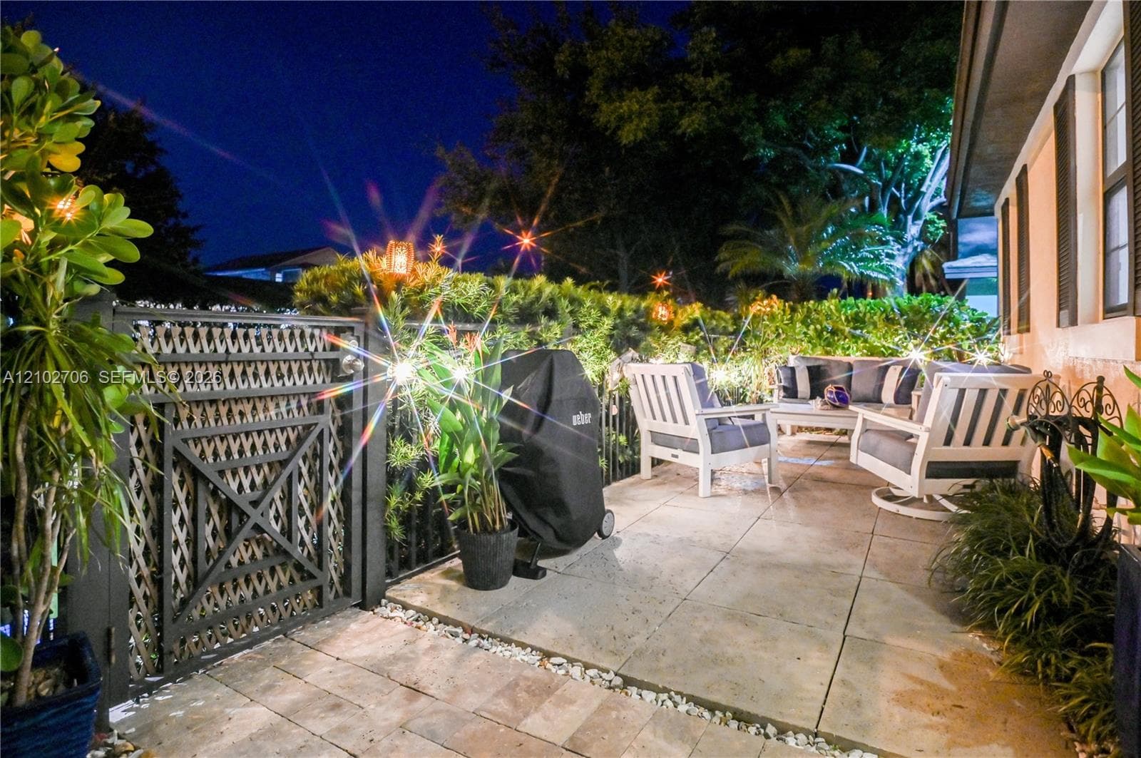 Paver patio featuring a decorative metal gate, manicured privacy hedging, and professional landscape lighting