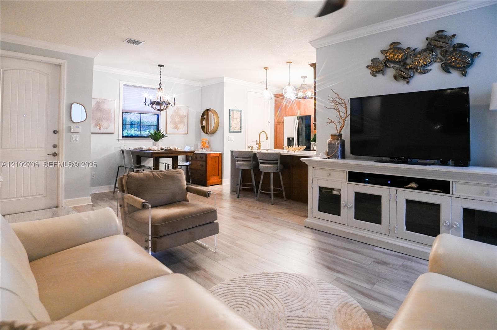 Open-concept interior featuring light wood-finish flooring, crown molding, a kitchen island with pendant lighting, and a neutral color palette