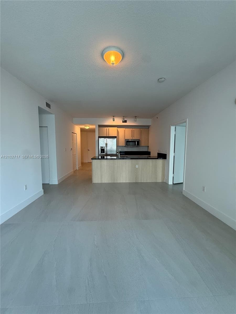 Open-concept interior featuring large-format tile flooring, flat-panel cabinetry, a kitchen island with stone-finish countertops, and stainless steel kitchen appliances