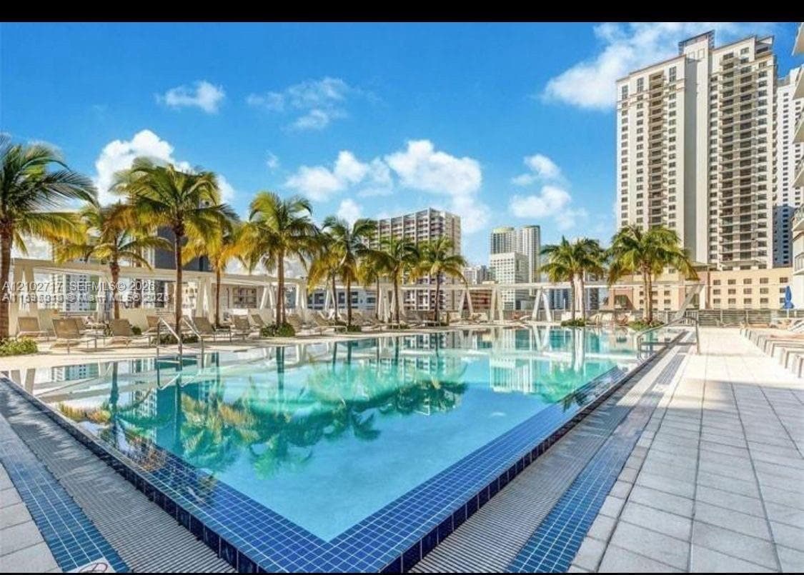 Outdoor swimming pool featuring a tiled perimeter, integrated palm trees, and stone-paver decking