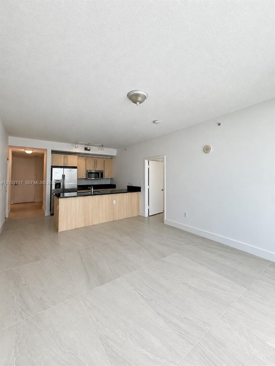 Large-format tile flooring, kitchen featuring wood-finish cabinetry, stone-surface countertops, and stainless steel appliances
