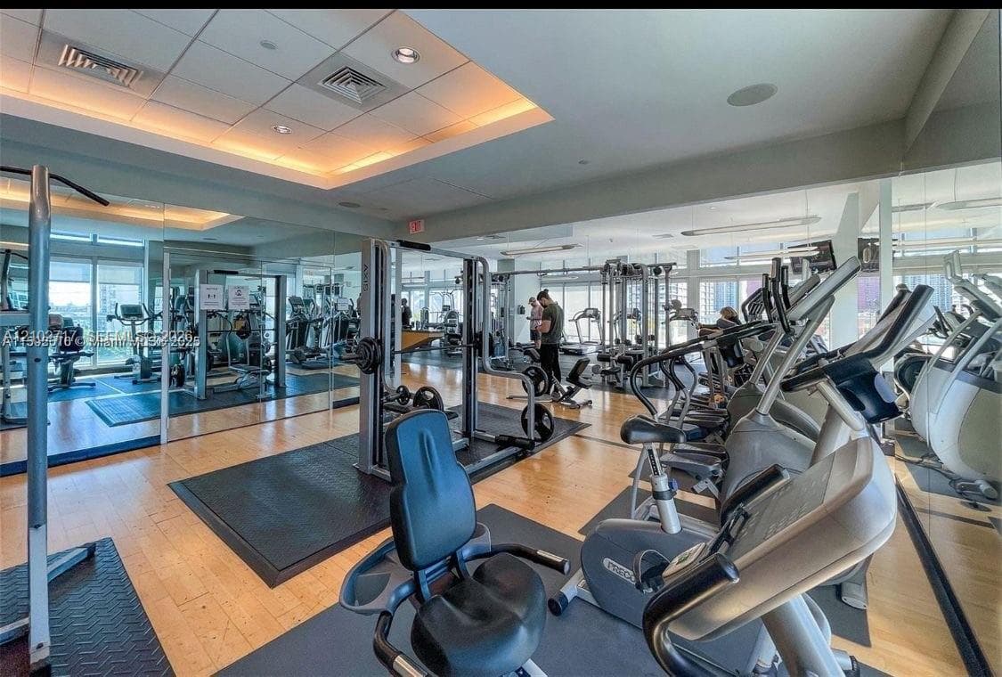 Fitness center featuring wood-finish flooring, floor-to-ceiling mirrored walls, recessed tray ceiling lighting, and expansive windows