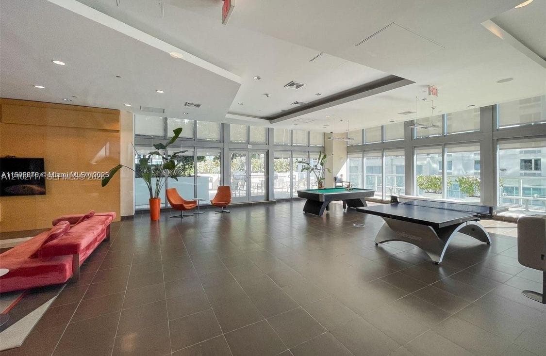 Spacious multi-use area featuring recessed lighting, tile flooring, soaring tray ceilings, and an extensive wall of floor-to-ceiling windows
