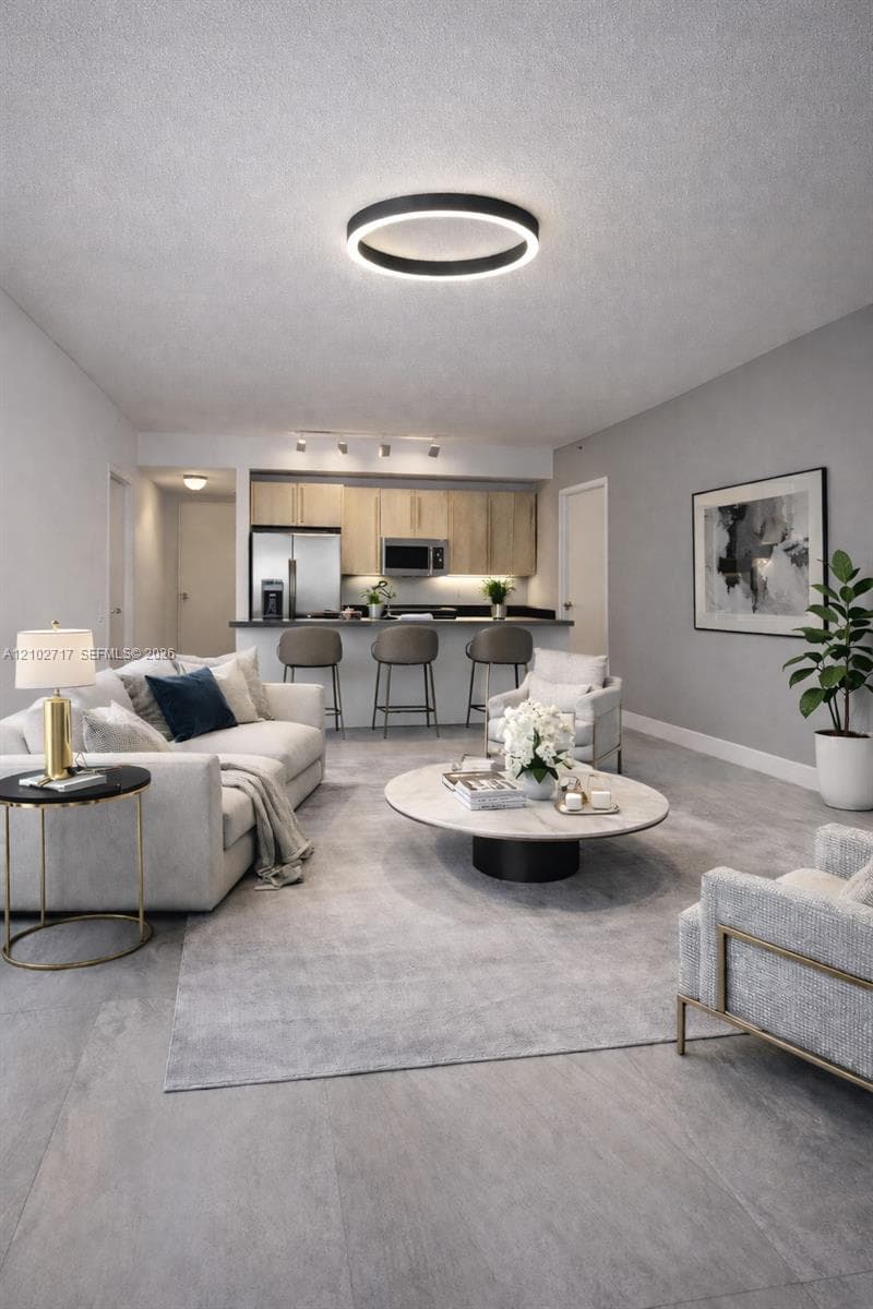 Open-concept floor plan featuring large-format tile flooring, a breakfast bar, wood-finish cabinetry, and a circular LED flush-mount light fixture