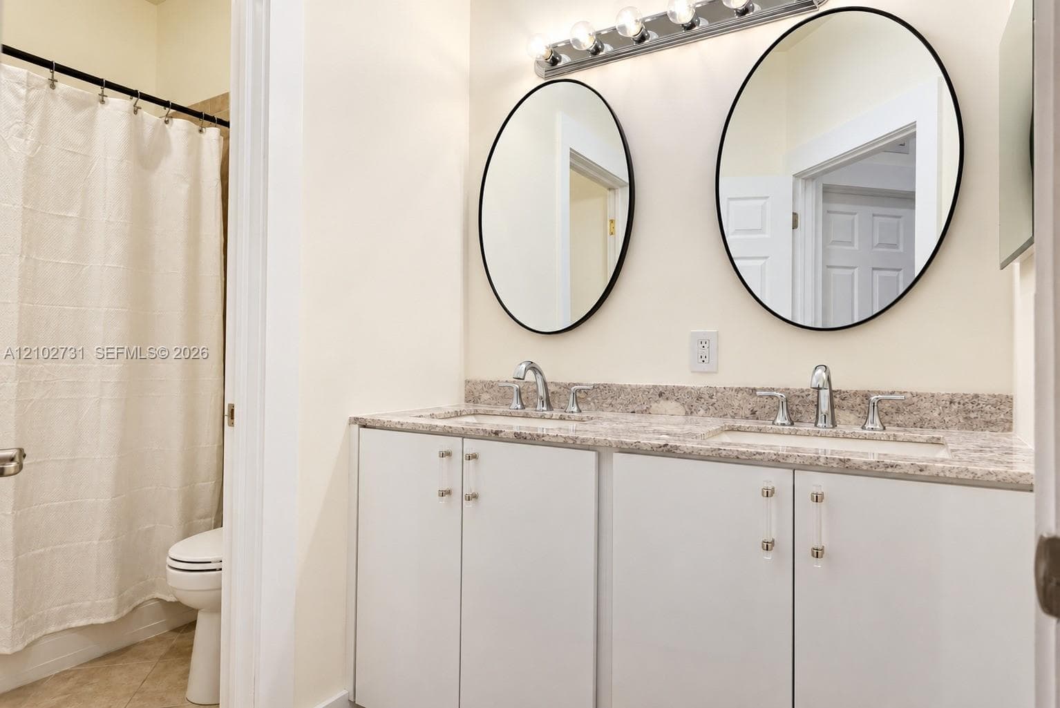 Dual-sink vanity featuring stone-composite countertops, undermount sinks, polished chrome fixtures, dual oval mirrors with black frames, and modern cabinet hardware