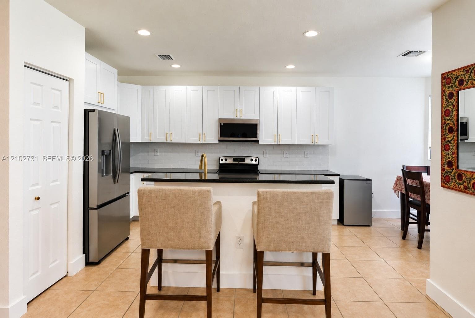Kitchen featuring white shaker-style cabinetry, a dark stone countertop peninsula, stainless steel appliances, and tile flooring