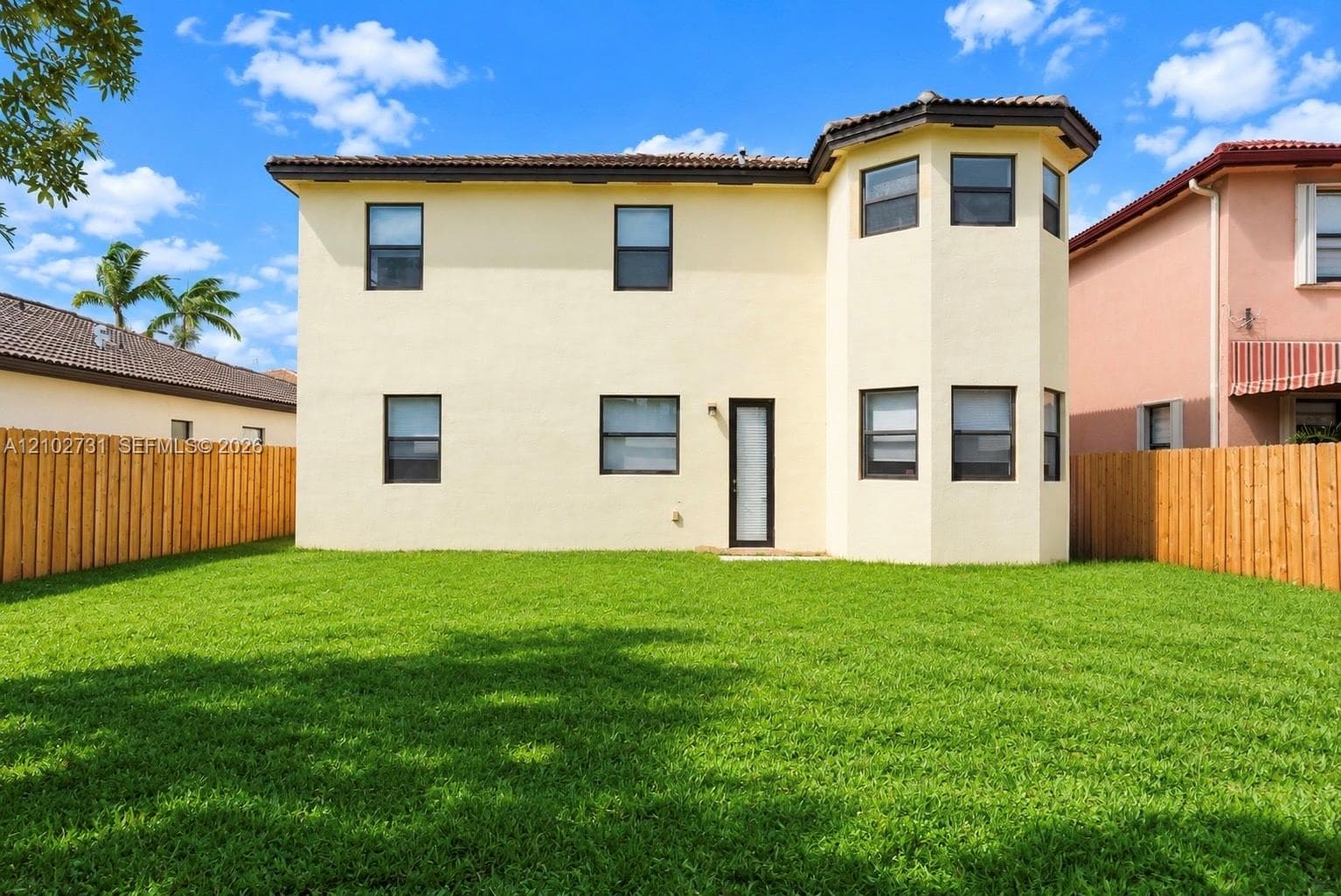 Two-story exterior featuring a stucco facade, multi-faceted architectural bay, tile roof, and enclosed fenced backyard with lawn