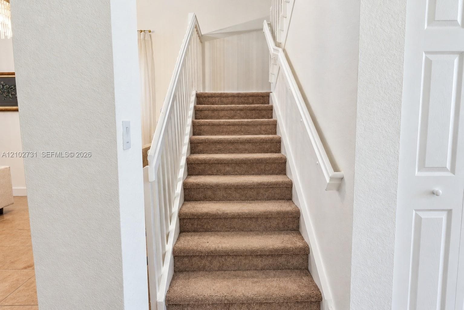 Staircase featuring neutral carpeting, white wooden balusters, a matching handrail, and a paneled closet door