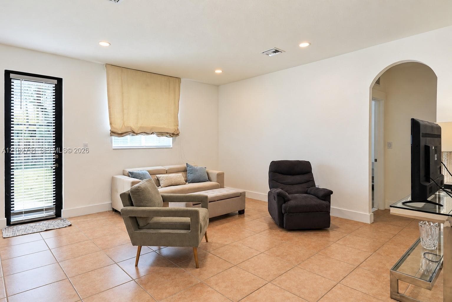 Interior space featuring neutral wall tones, ceramic tile flooring, recessed ceiling lighting, a glass-panel door with integrated blinds, and an arched entryway
