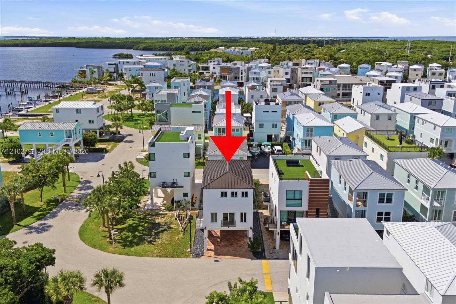 Elevated residence with a metal roof, paver driveway, and balcony, situated in a coastal waterfront community