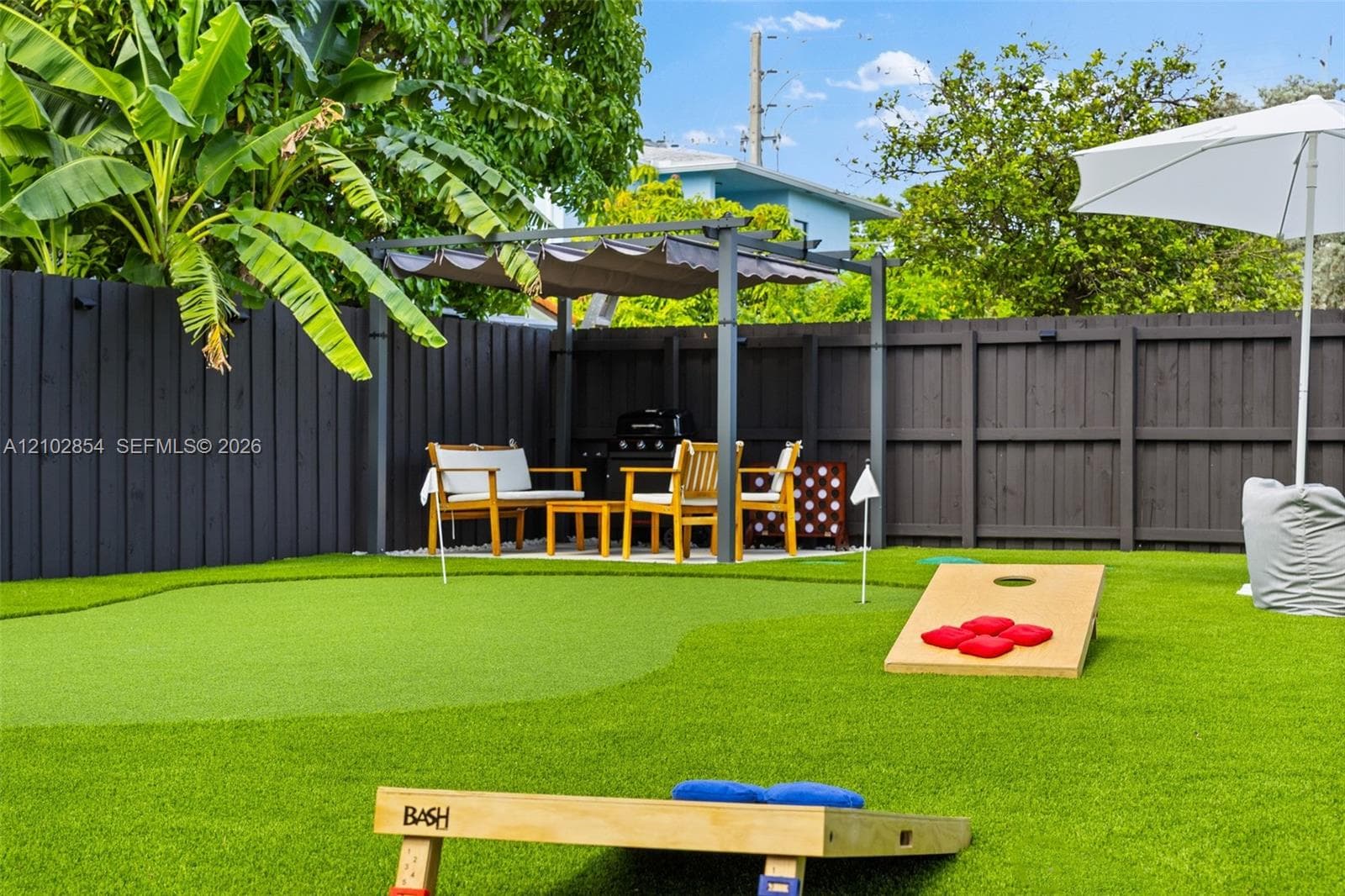 Fenced backyard featuring synthetic turf, a built-in putting green, and a metal-frame pergola with retractable canopy