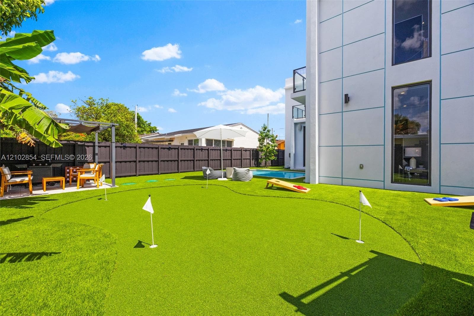 Private backyard featuring a synthetic putting green, in-ground swimming pool, metal-framed covered patio, and perimeter privacy fencing
