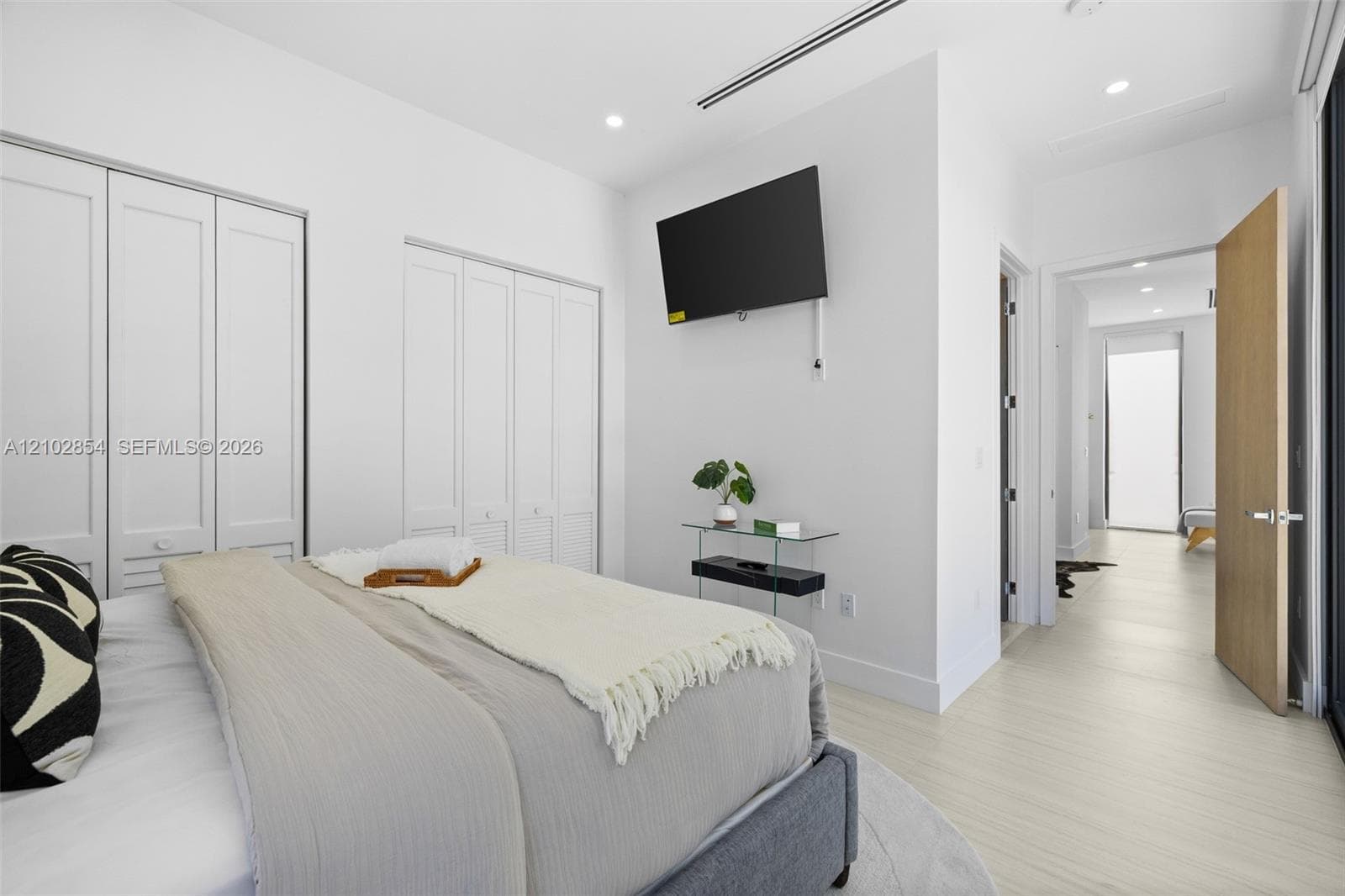 Floor-to-ceiling bi-fold closet doors, recessed ceiling lighting, linear HVAC diffusers, and wood-finish flooring