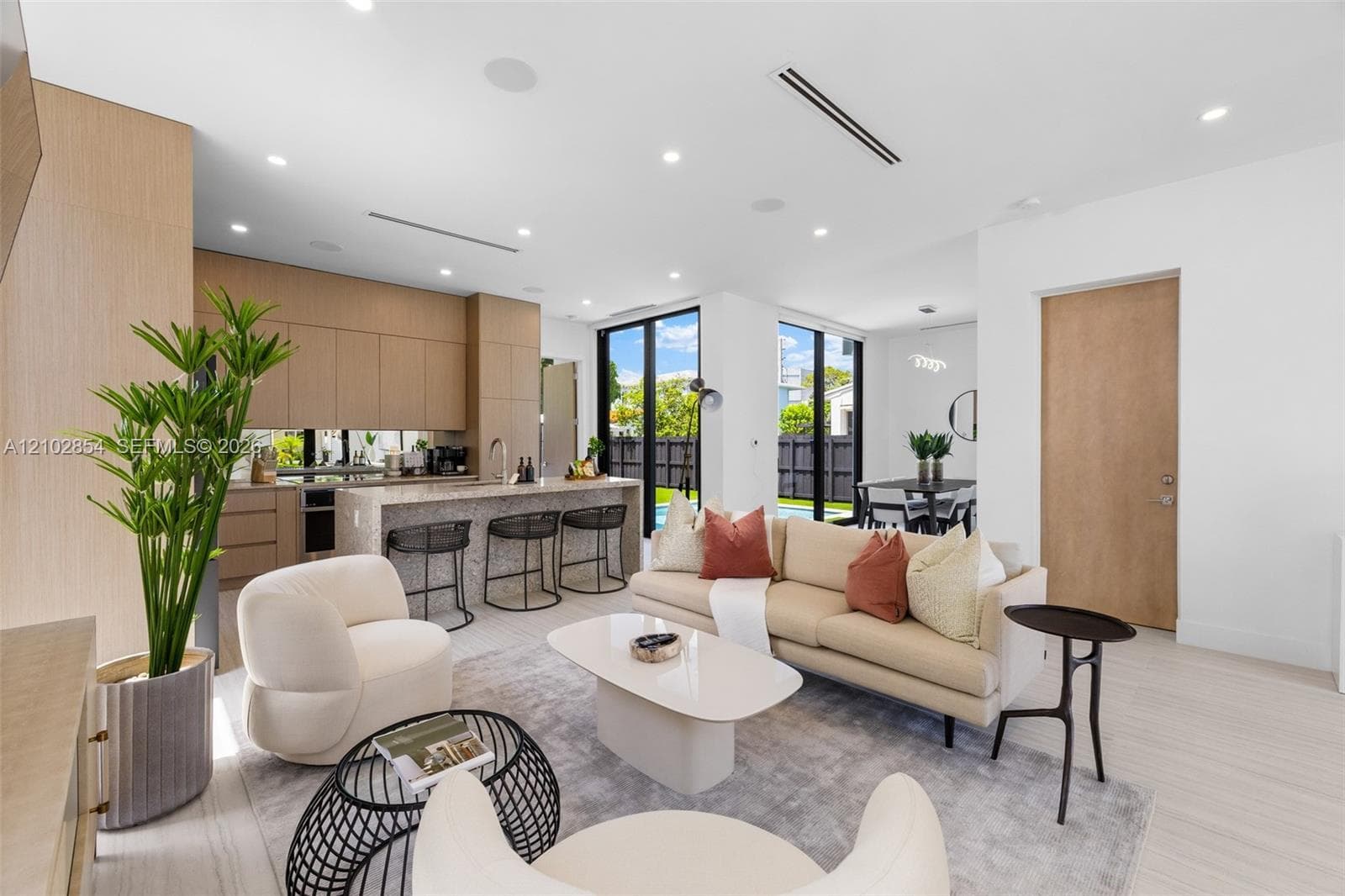 Open-concept area featuring light wood-finish cabinetry, a stone-topped island with seating, recessed ceiling lighting, and floor-to-ceiling windows