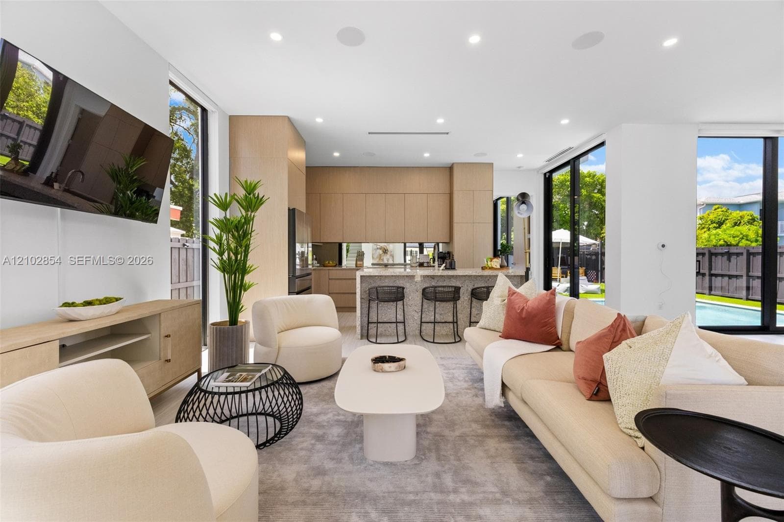 Open-concept interior featuring light wood-finish cabinetry, floor-to-ceiling windows, recessed lighting, and a kitchen island with a stone-finish countertop