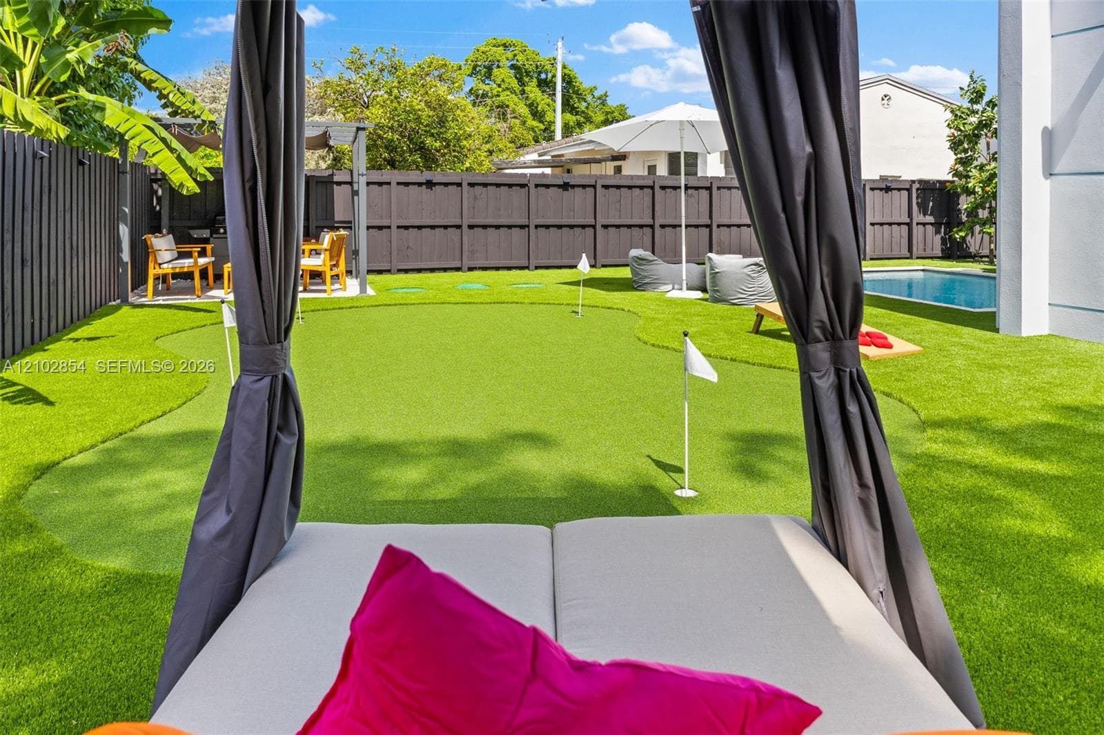 Backyard featuring a private putting green, swimming pool, dark wood-finish privacy fencing, and a hardscaped patio area