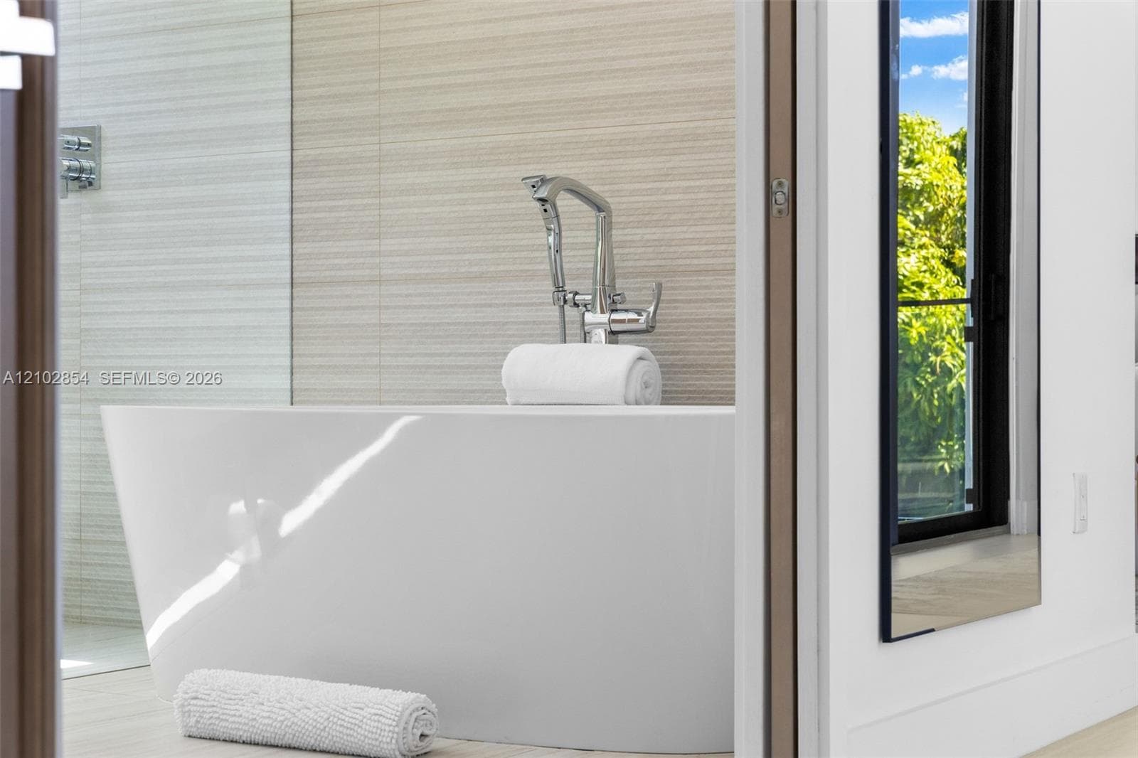 Freestanding soaking tub with a polished chrome floor-mounted faucet and textured tile wall accents