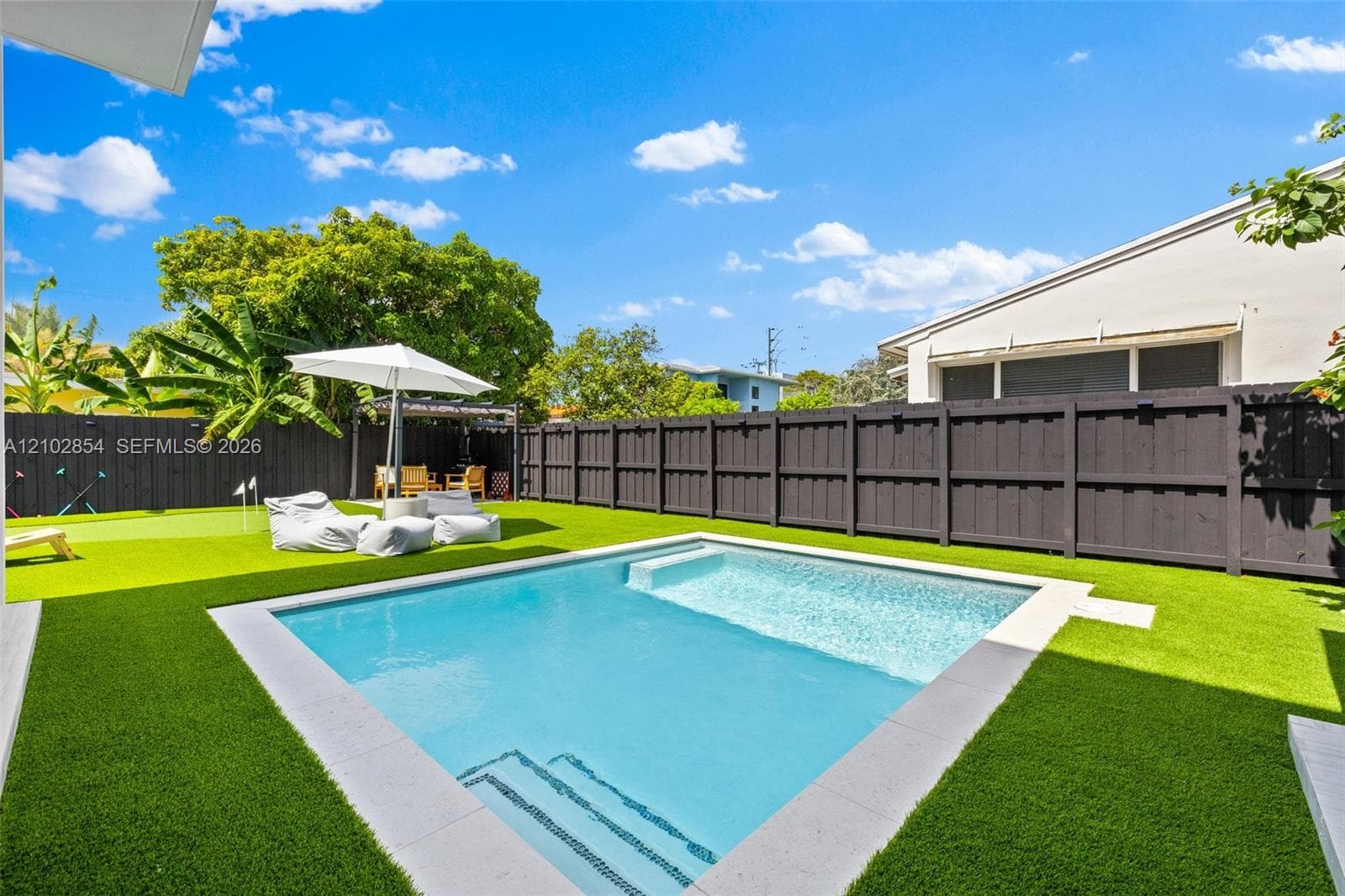 Backyard featuring a swimming pool with a sun shelf, synthetic turf lawn, putting green, and perimeter privacy fencing