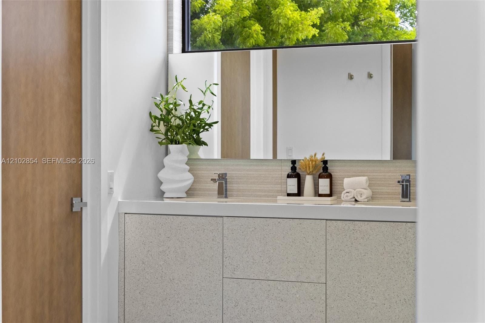 Floating vanity with textured cabinetry, solid surface countertop, linear tile backsplash, horizontal mirror, and chrome dual-faucet fixtures
