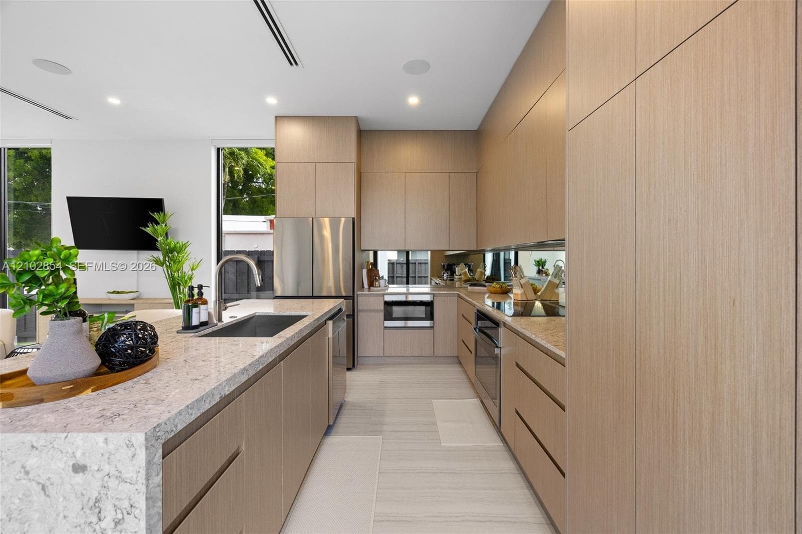 Kitchen featuring flat-panel wood-finish cabinetry, quartz countertops, stainless steel appliances, a mirrored backsplash, and recessed lighting