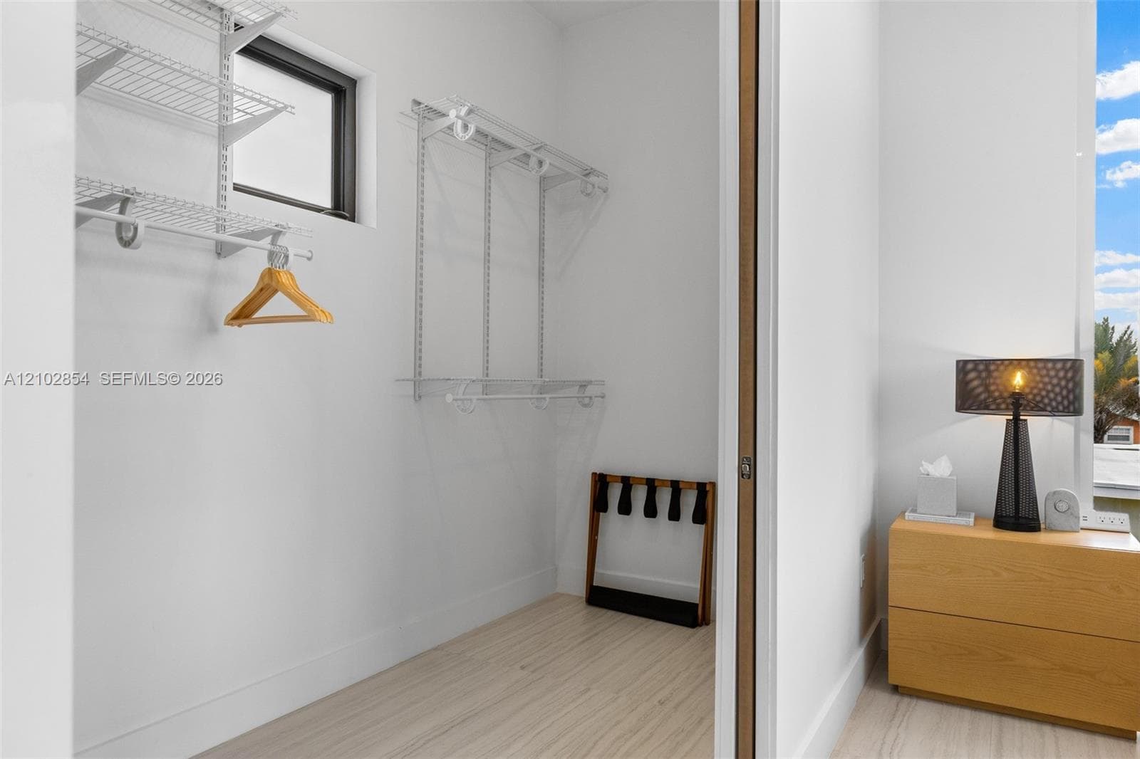 Storage space featuring white wire shelving units, light-toned wood-finish flooring, and a window providing natural light