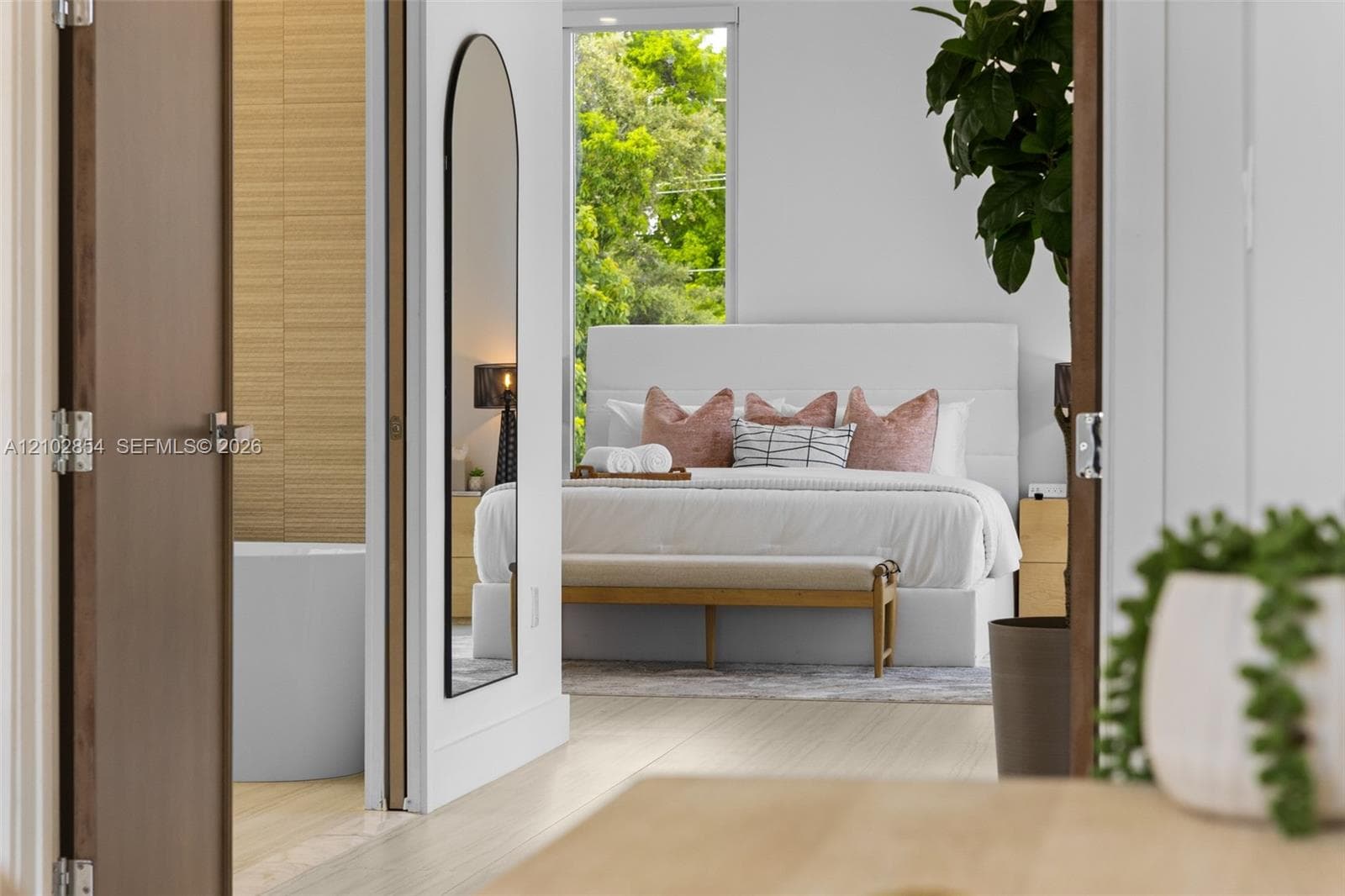 Solid wood-finish door, tall arched-top wall mirror with a thin black frame, wood-finish flooring, and a large floor-to-ceiling rectangular window