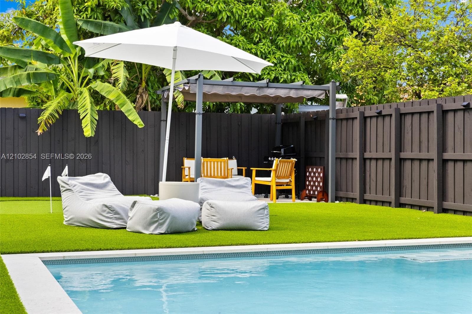 Backyard featuring a swimming pool, synthetic turf, metal pergola, and perimeter wood privacy fencing