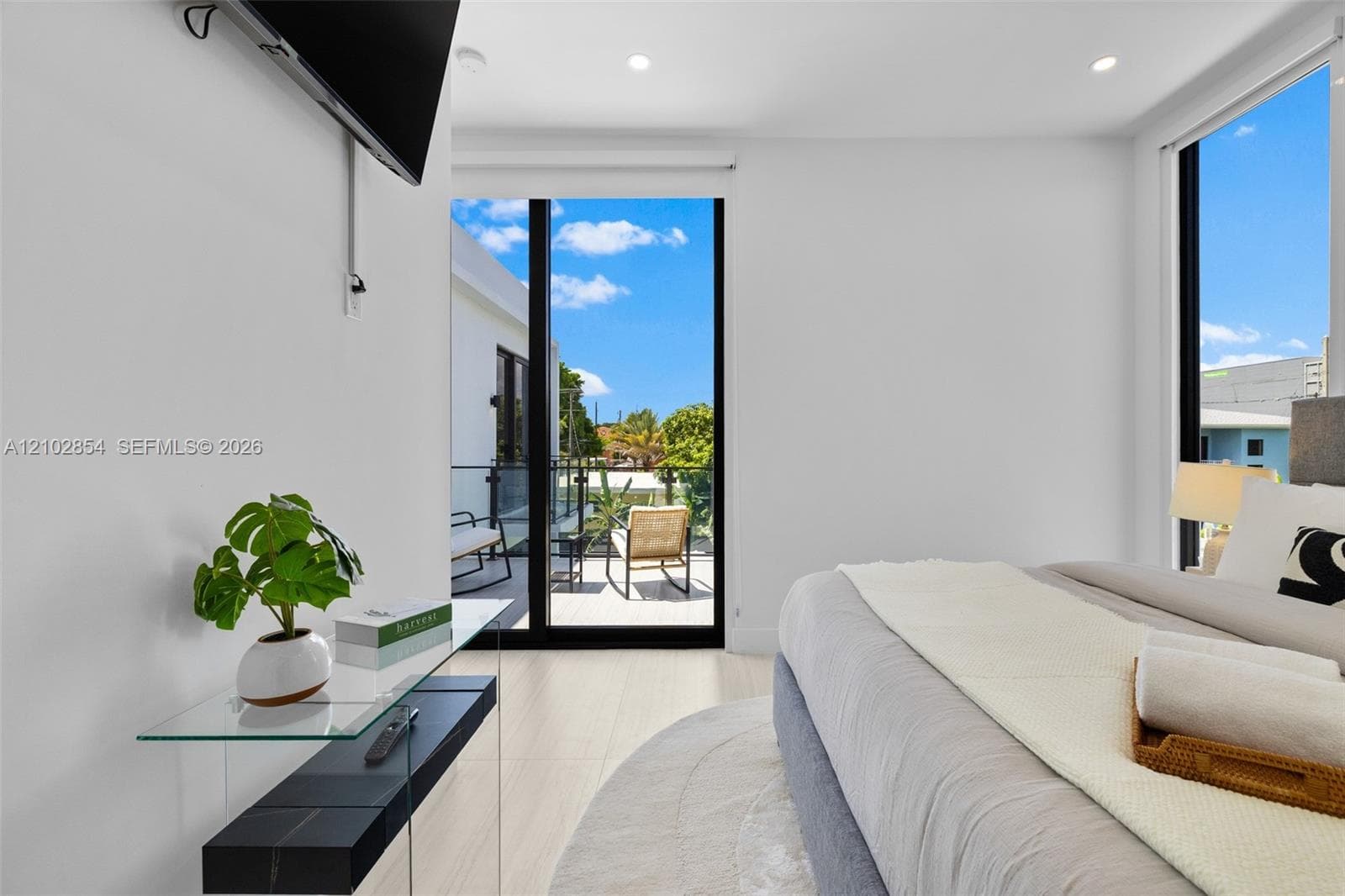 Light-filled room featuring large sliding glass doors, a glass-railed exterior balcony, neutral tile flooring, and recessed ceiling lighting