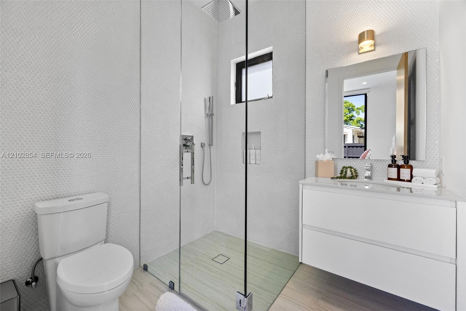 Walk-in shower with a glass enclosure, rainfall showerhead, and built-in wall niche, paired with a white floating vanity and a sleek wall-mounted light fixture