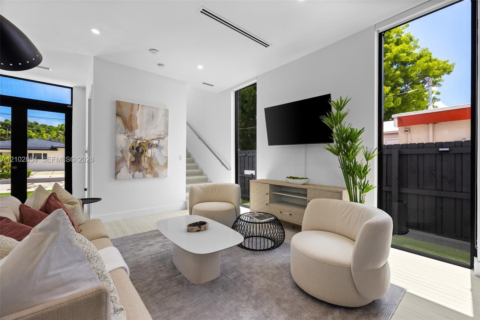 Living area featuring floor-to-ceiling windows, high-contrast black window frames, recessed lighting, and sleek wood-finish flooring