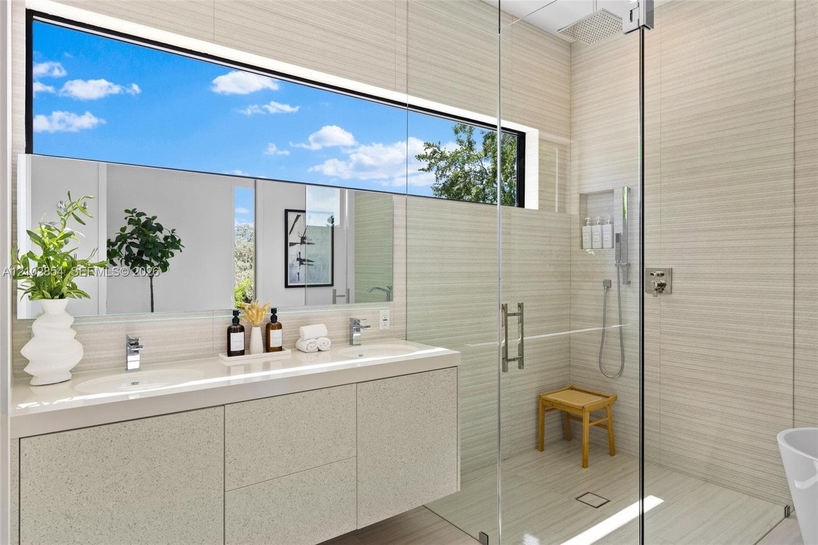 Floating dual-sink vanity with a solid-surface countertop, full-width mirror, walk-in shower with floor-to-ceiling tile, glass enclosure, and high-set horizontal window