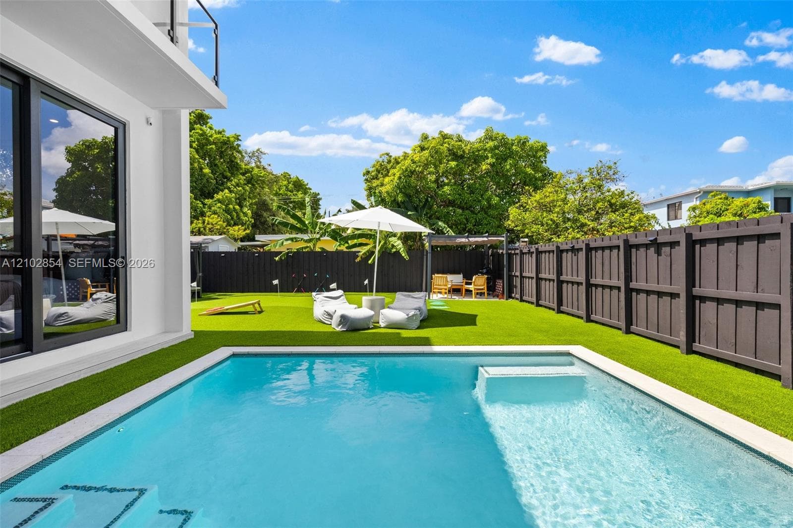 Private backyard featuring a rectangular swimming pool with a sun shelf, synthetic turf lawn, and full-perimeter horizontal wood-style fencing