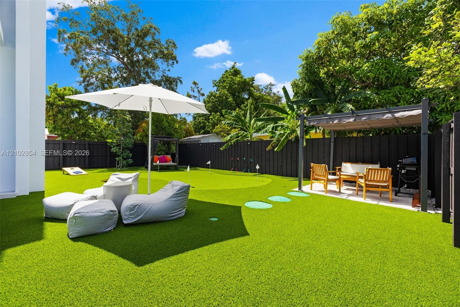 Rear exterior space featuring a synthetic turf surface, integrated putting green, overhead pergola structure, and privacy fencing