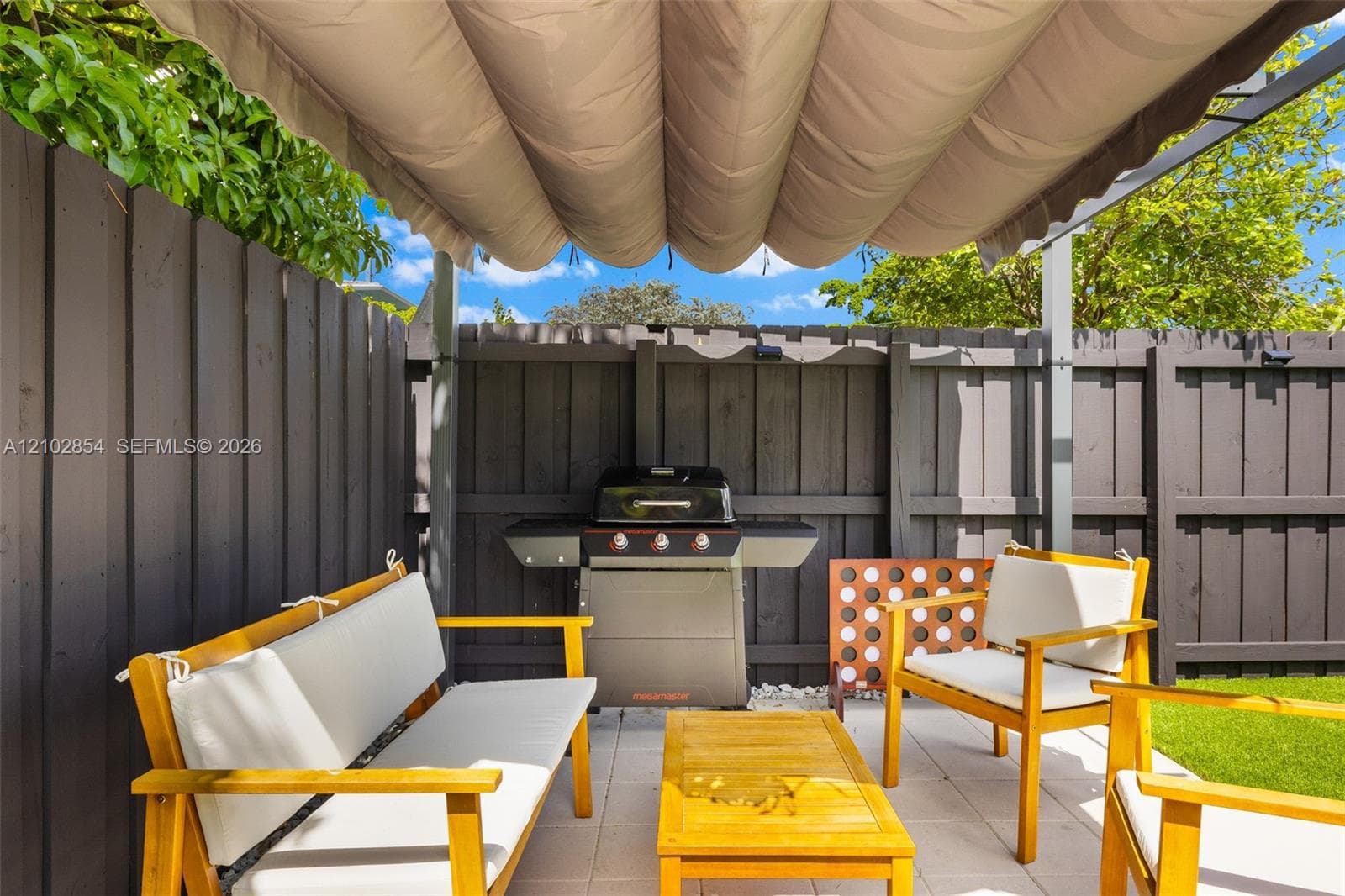 Outdoor living space featuring a retractable fabric canopy, paved patio, dark wood-finish privacy fencing, and a built-in outdoor gas grill