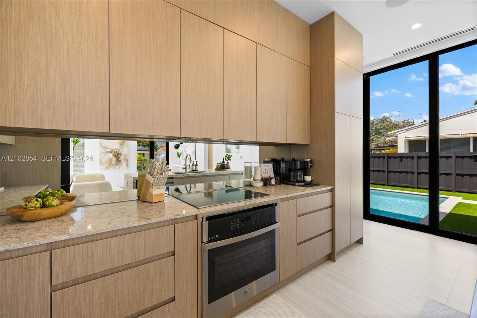 Kitchen featuring light-toned cabinetry, stone countertops, a mirrored backsplash, a built-in wall oven with a cooktop, and floor-to-ceiling glass doors
