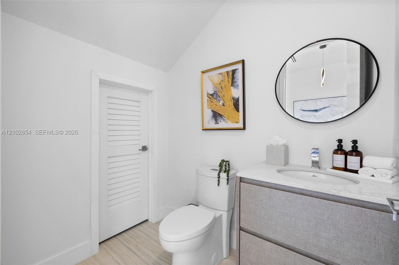 Floating vanity with a light-toned stone countertop, integrated sink, matte chrome faucet, oval wall-mounted mirror with a black frame, and a white louvered door